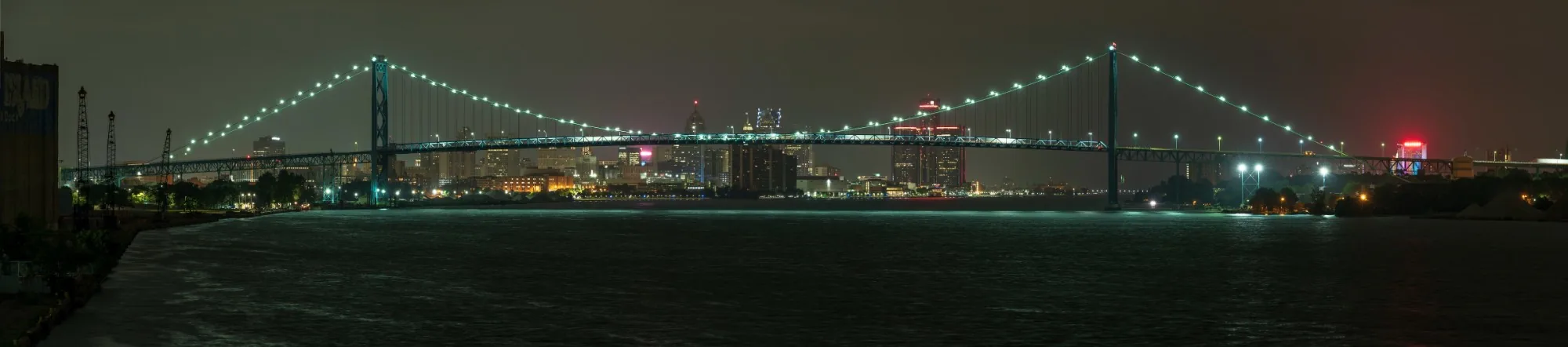The Detroit skyline and the Ambassador Bridge lit up at night, seen across the river